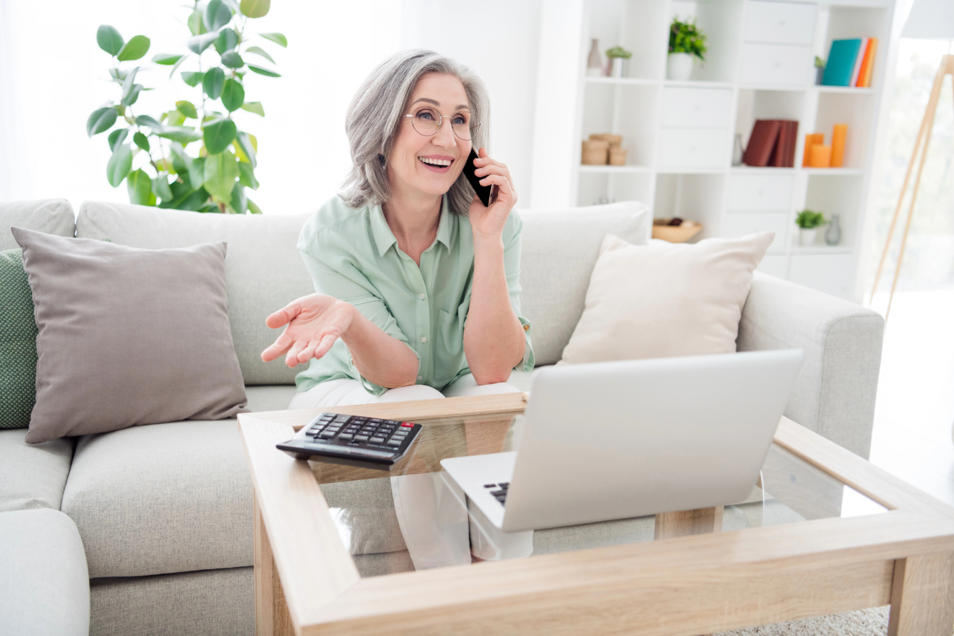 Photo of cheerful person sit on couch speak phone arm palm explain tell have good mood toothy smile indoors Photo of cheerful person sit on couch speak phone arm palm explain tell have good mood toothy smile indoors.